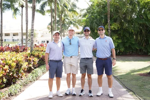 Four golfers pose together outside among palm trees.