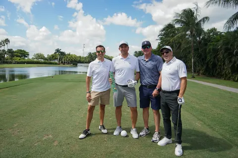 Four golfers pose beside the course and water.