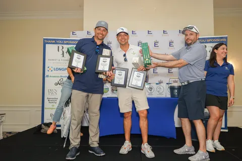 A group poses with framed awards in front of the tournament backdrop.